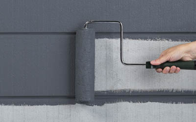 Closeup of a person’s hand using a roller to apply dark gray paint