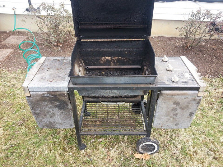 A gas grill with the top open and dirty metal around it. 