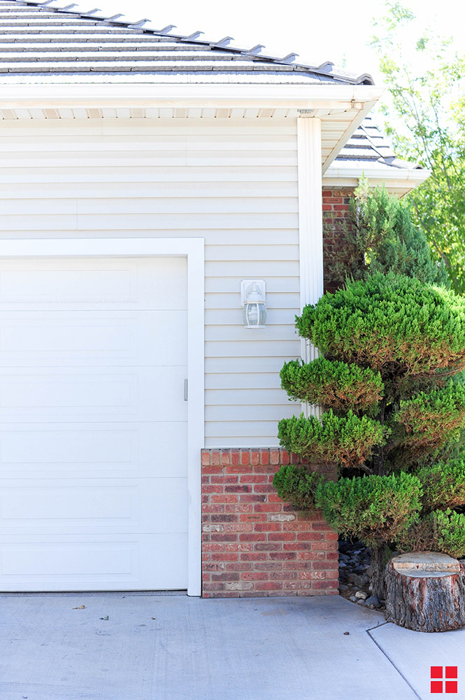 The side of a white garage door on a garage with gray siding and brick below it.